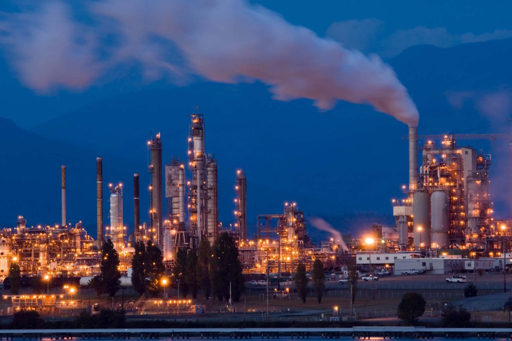 Illuminated refinery towers at twilight, with steam rising from a stack, managed by ResponsAble safety staffing.