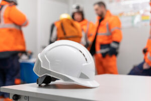 White safety helmet on a table with construction crew in high-visibility gear blurred in the background, symbolizing workplace safety protocols and change management.