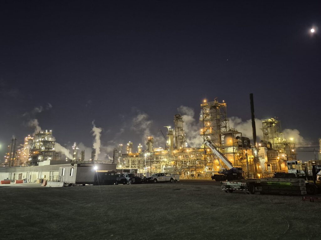 Refinery at night with steel towers, steam vents, and trucks, reflecting ResponsAble industrial safety staffing.