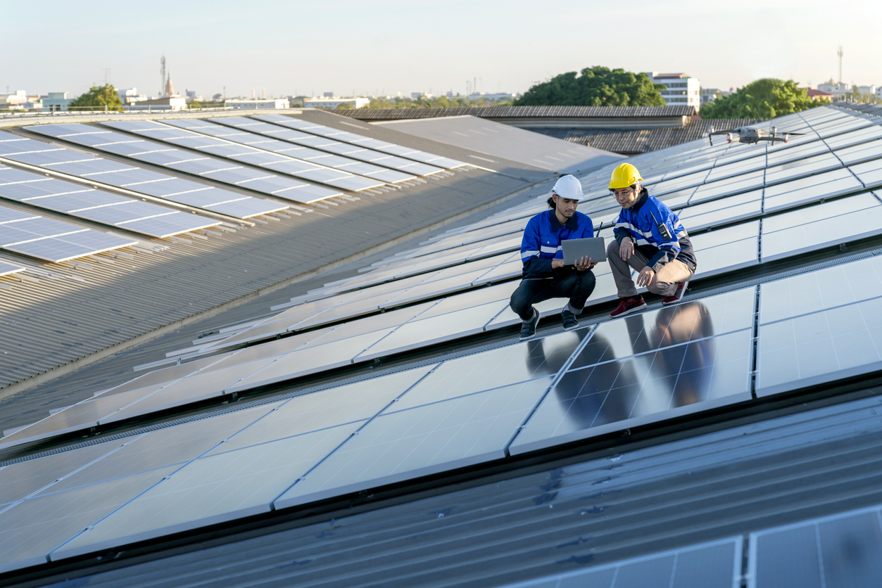 Specialist technician professional engineer with laptop and tablet maintenance checking installing solar roof panel on the factory rooftop under sunlight. Engineers team survey check solar panel roof. Specialist technician professional engineer with laptop and tablet maintenance checking installing solar roof panel on the factory rooftop under sunlight. Engineers team survey check solar panel roof.