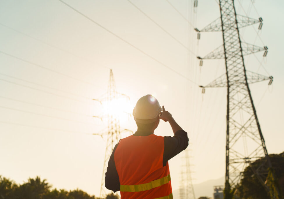 Power industry specialist beside transmission towers at sunset, representing energy security, resilience, industrial safety culture and the role in sustainable electricity futures ahead.